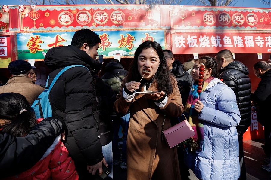 A woman eats at a street food stall during a temple fair at a park in Beijing, China, on 10 February 2024.  (Tingshu Wang/Reuters)