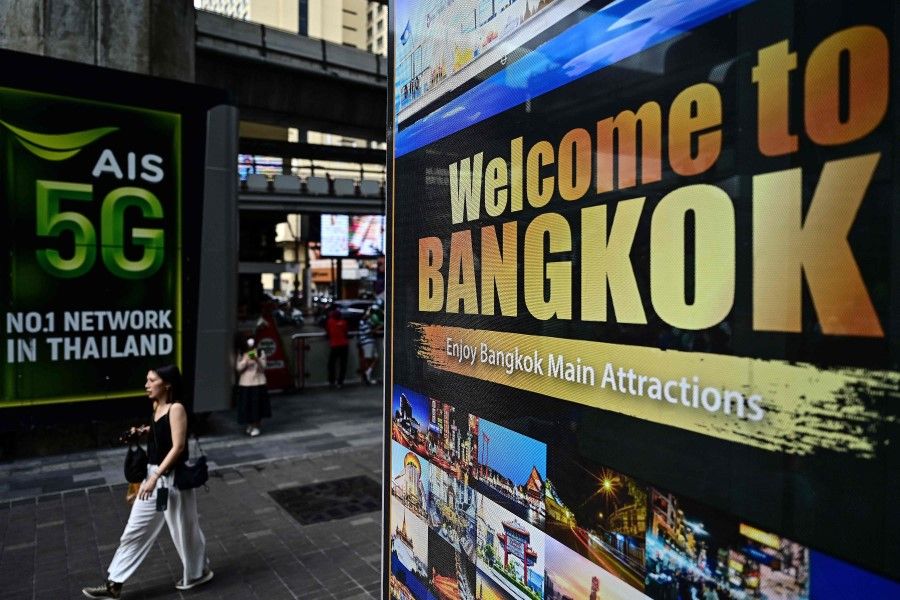 This photo taken on 17 March 2023 shows a woman walking past a sign highlighting tourist attractions in Bangkok. (Manan Vatsyayana/AFP)