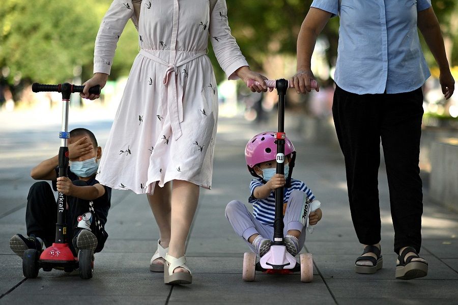 Children ride on kick scooters pulled along by adults in Beijing, China, on 27 August 2021. (Noel Celis/AFP)