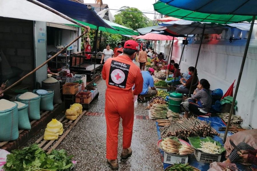 A Laos Red Cross volunteer raises awareness on the symptoms of COVID-19 and the means to protect oneself from it, in a market in Vientiane, Laos, 30 April 2020. (Laos Red Cross/Handout via REUTERS)