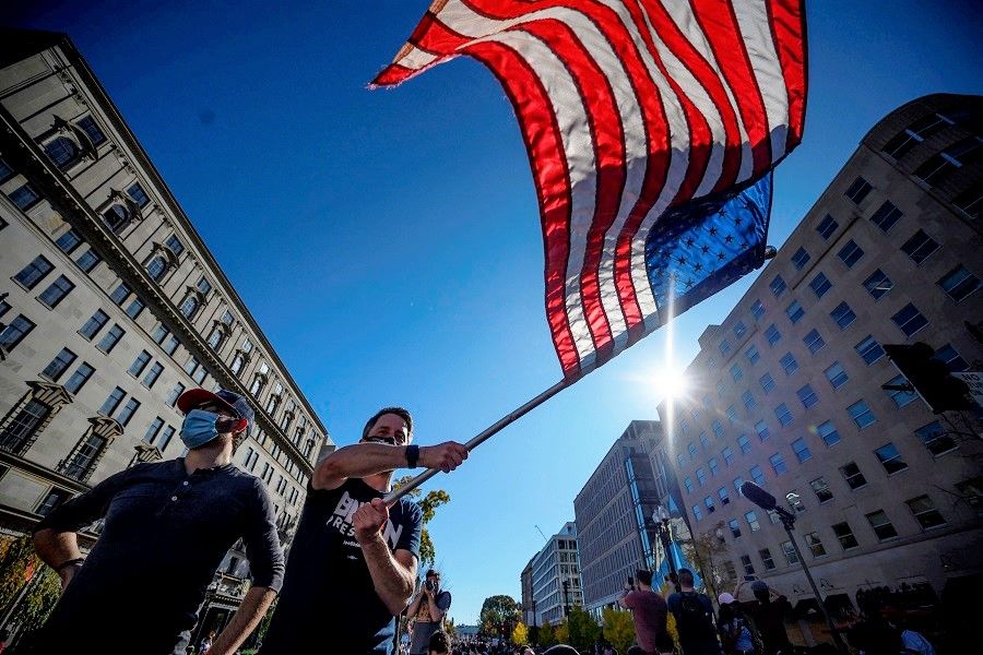 A man waves a US flag as people celebrate on Black Lives Matter plaza across from the White House in Washington, DC on 7 November 2020, after Joe Biden was declared the winner of the 2020 presidential election. (Eric Baradat/AFP)