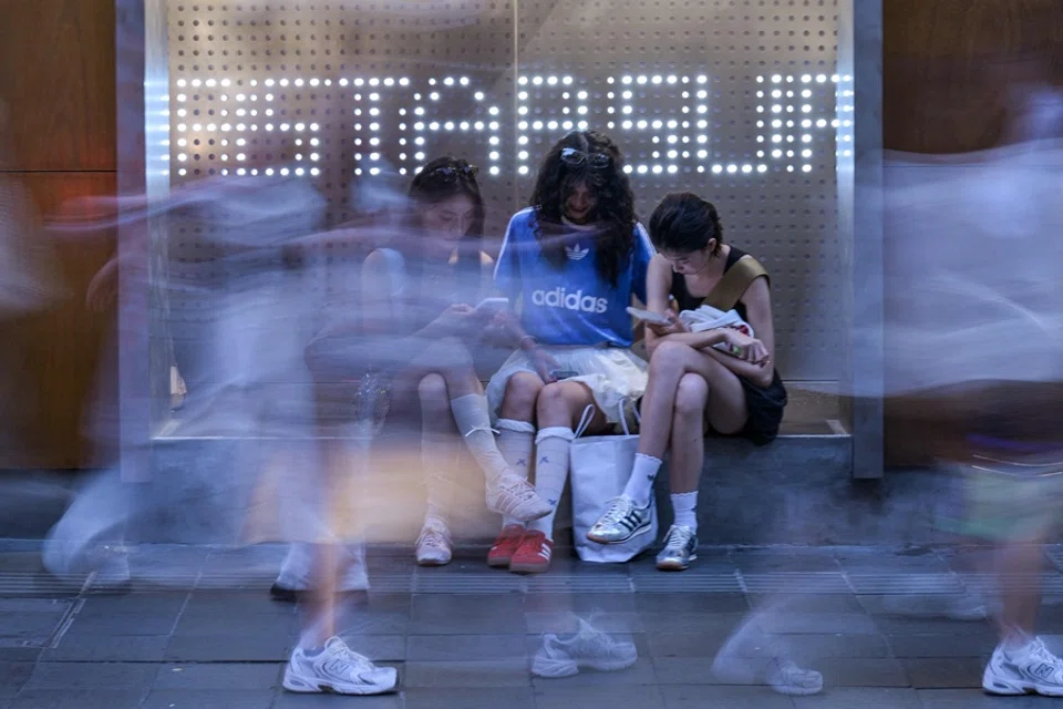 Young women sit outside an Adidas store while people walk on a street in the Xuhui district in Shanghai on 22 May 2025.  (Hector Retamal/AFP)