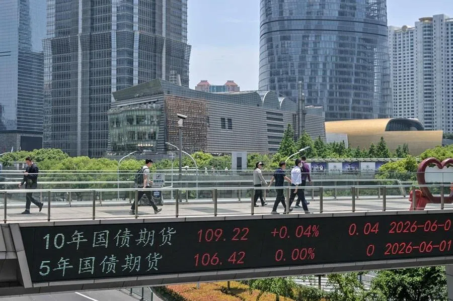 People walk on a footbridge with a screen displaying the treasury bond futures index at the financial district of Lujiazui in Shanghai, China, on 1 June 2026.