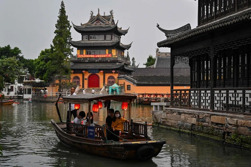 This photo taken on 24 July 2022 shows a man sailing a boat with tourists along a channel in the Zhujiajiao ancient water town in Shanghai, China. (Hector Retamal/AFP)