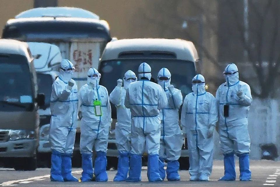 Workers in protective suits after loading travellers onto buses outside the New China International Exhibition Centre, near Beijing Capital Airport in Beijing, 17 March 2020. The exhibition center is being used as a registration and screening centre for travellers arriving in Beijing before transferring them to quarantine locations. (Greg Baker/AFP)