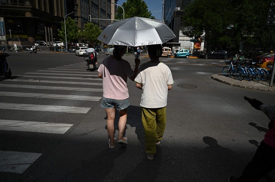 People cross a road in Beijing, China, on 7 July 2023. (Greg Baker/AFP)