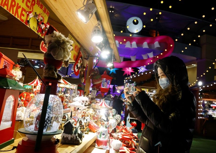 A woman wearing a face mask takes a picture of a display at a Christmas market in a shopping mall following an outbreak of the coronavirus disease (COVID-19) in Beijing, 16 December 2020. (Thomas Peter/Reuters)