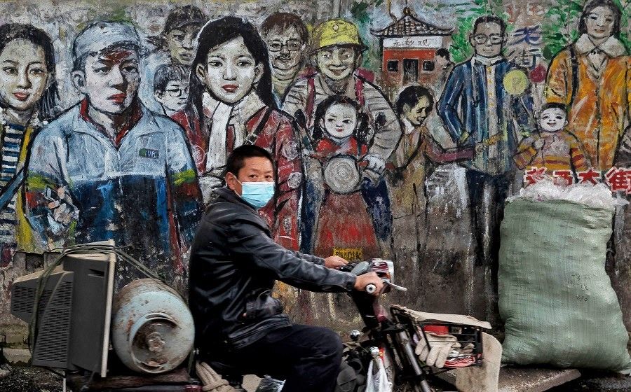 A man wearing a face mask amid the Covid-19 pandemic drives his motorbike along a street in Wuhan, China, on 24 April 2020. (STR/AFP)