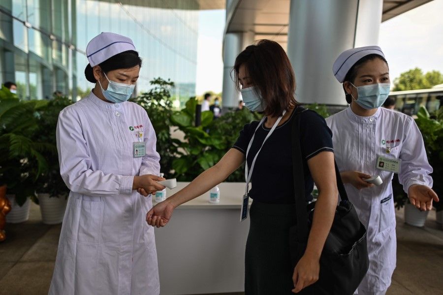 A medical worker takes the temperature of arriving people at Tongji Hospital in Wuhan, China's central Hubei province on 3 September 2020, during a media visit to the facility organised by local authorities. (Hector Retamal/AFP)