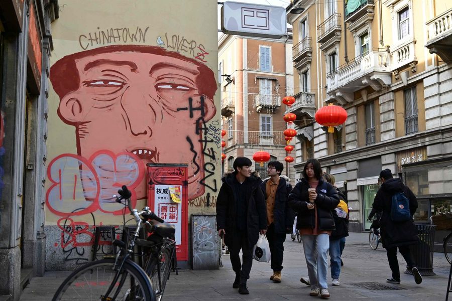 People pass by a mural depicting a Chinese face in Via Paolo Sarpi, the commercial street of the Chinese district of Milan on 30 January 2020. (Miguel Medina/AFP)