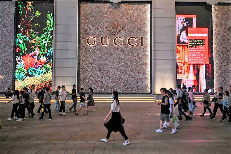 This photo taken on 25 May 2021 shows people walking past a designer shop in Shanghai, China. (Hector Retamal/AFP)