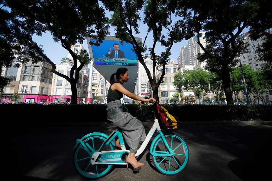 A woman cycles past a screen showing a news conference by Chinese Premier Li Keqiang after the closing session of the National People's Congress, in Beijing, China, on 28 May 2020. (Thomas Peter/Reuters)