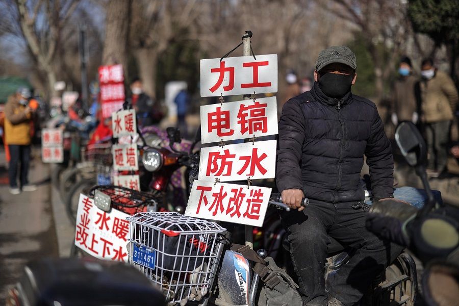 A day labourer wearing a face mask sits next to a sign advertising his skills as he waits to get hired for renovation works in Shenyang, Liaoning province on 27 March 2020. (STR/AFP)