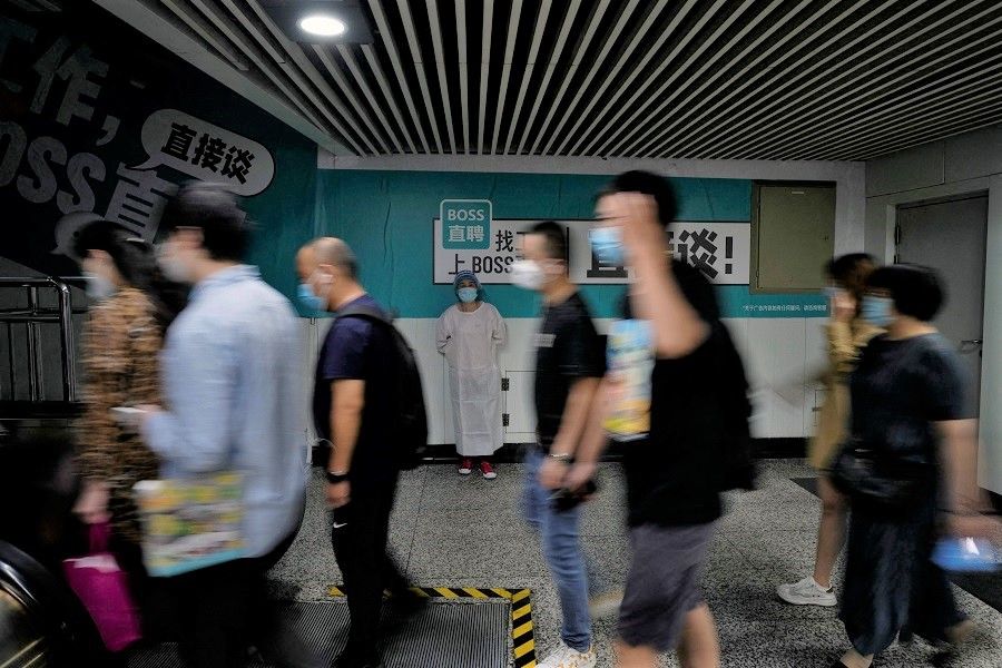 A worker in a protective suit stands near commuters at a subway station in Shanghai, China, 2 June 2022. (Aly Song/Reuters)