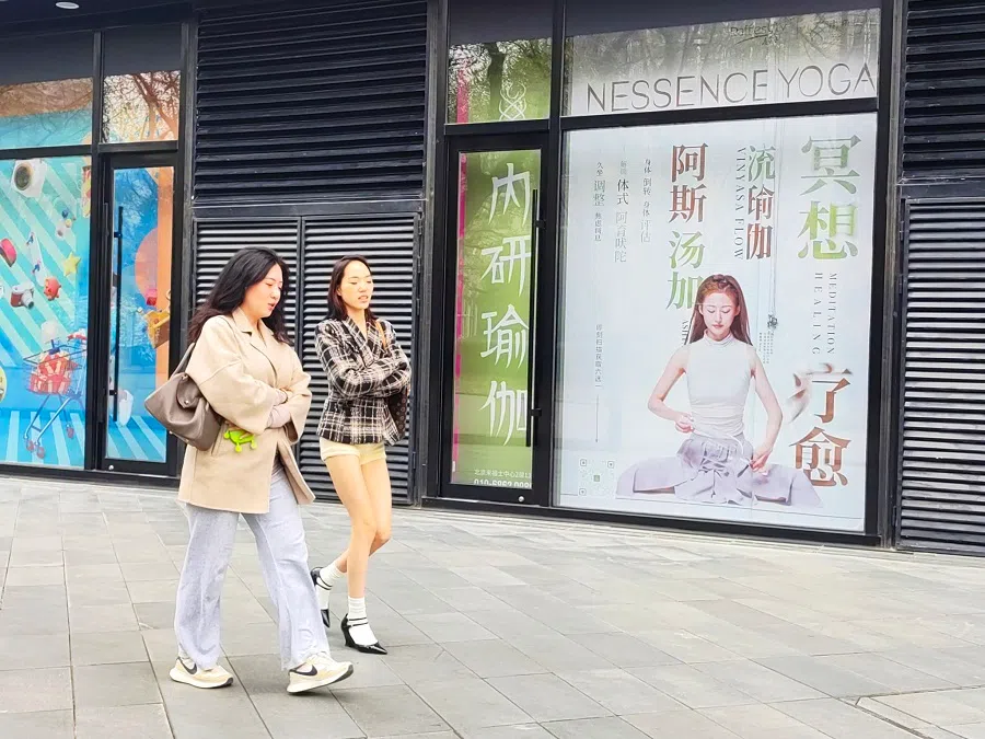 Youth walk on the street past an advertisement of a yoga studio in Beijing’s Raffles City Shopping Centre. 