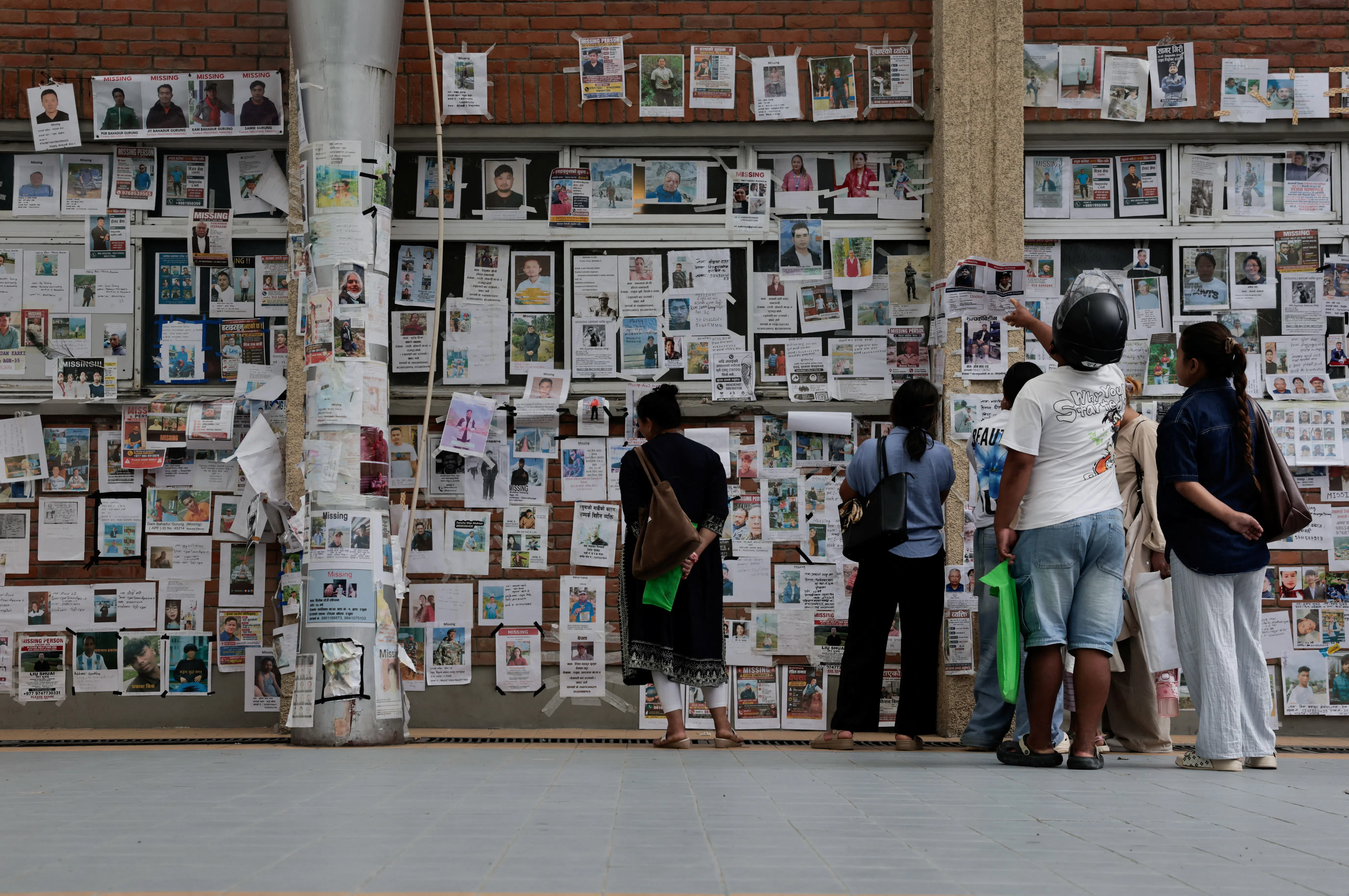 People look at photographs of missing people on a wall outside Tribhuvan University Teaching Hospital following the deadly flash floods and mudslide, in Kathmandu, Nepal, 16 September 2026.