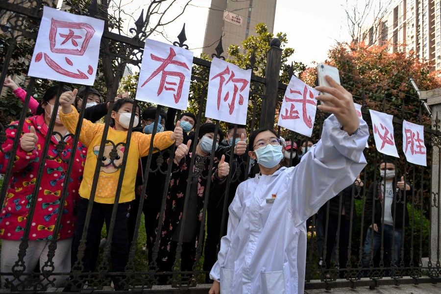 A member of a medical assistance team from Yunnan province taking a selfie with Wuhan residents who set up banners of appreciation as the team departs Wuhan, 18 March 2020. The full banner reads "Appreciate having you. Wuhan will win!" (感恩有你，武汉必胜). (STR/AFP)