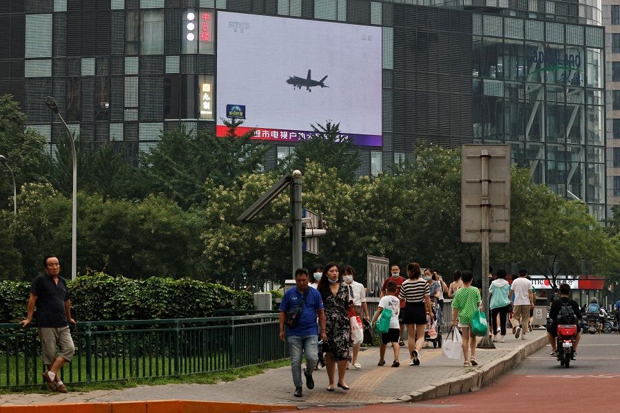 Pedestrians walk past a giant screen broadcasting a news report on Chinese People's Liberation Army (PLA)'s military exercises around Taiwan, in Beijing, China, 4 August 2022. (Thomas Peter/Reuters)