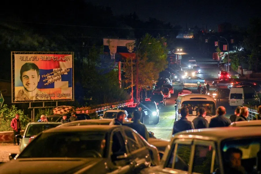 Residents in vehicles attempt to leave the city of Stepanakert following a military operation conducted by Azerbaijani armed forces in Nagorno-Karabakh, a region inhabited by ethnic Armenians, on 24 September 2023. A board in the background displays a Russian state flag and President Vladimir Putin. (David Ghahramanyan/Reuters)
