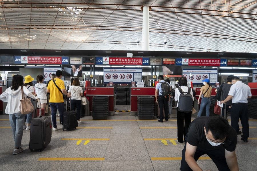Travelers observe social distancing measures while standing in line at baggage drop counters at Beijing Capital International Airport in Beijing, 6 July 2020. (Giulia Marchi/Bloomberg)