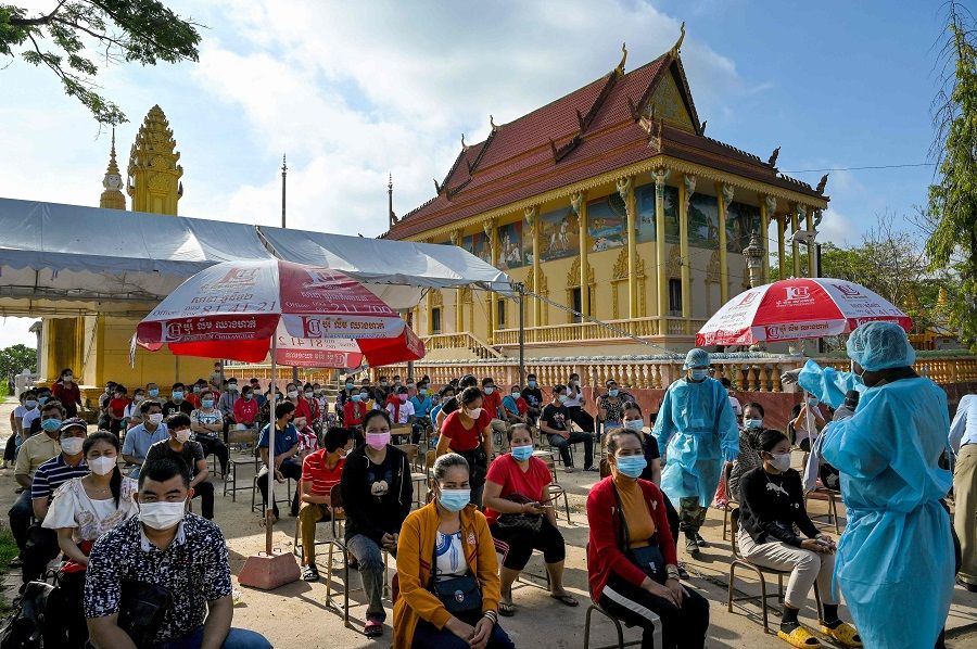 A soldier (right) gives instructions as people wait to receive the second dose of China's Sinopharm Covid-19 coronavirus vaccine at a pagoda in Phnom Penh, Cambodia on 20 May 2021. (Tang Chhin Sothy/AFP)
