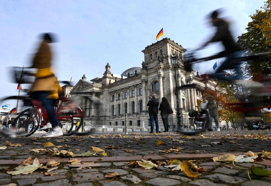 Leaves lay on the ground as pedestrians and bicycle riders are seen in front of the Reichstag building housing the lower house of parliament Bundestag in Berlin, Germany, on 19 October 2021. (Ina Fassbender/AFP)