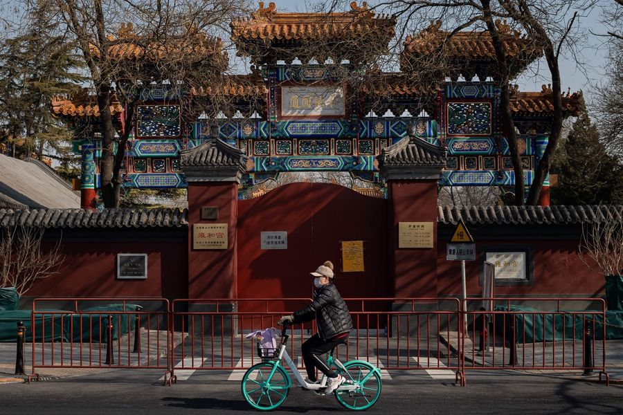 In this photo taken on 23 February 2020, a woman wearing a protective facemask to protect against the Covid-19 coronavirus cycles in front of the Lama Temple that is closed off to the public in Beijing. (Nicolas Asfouri/AFP)