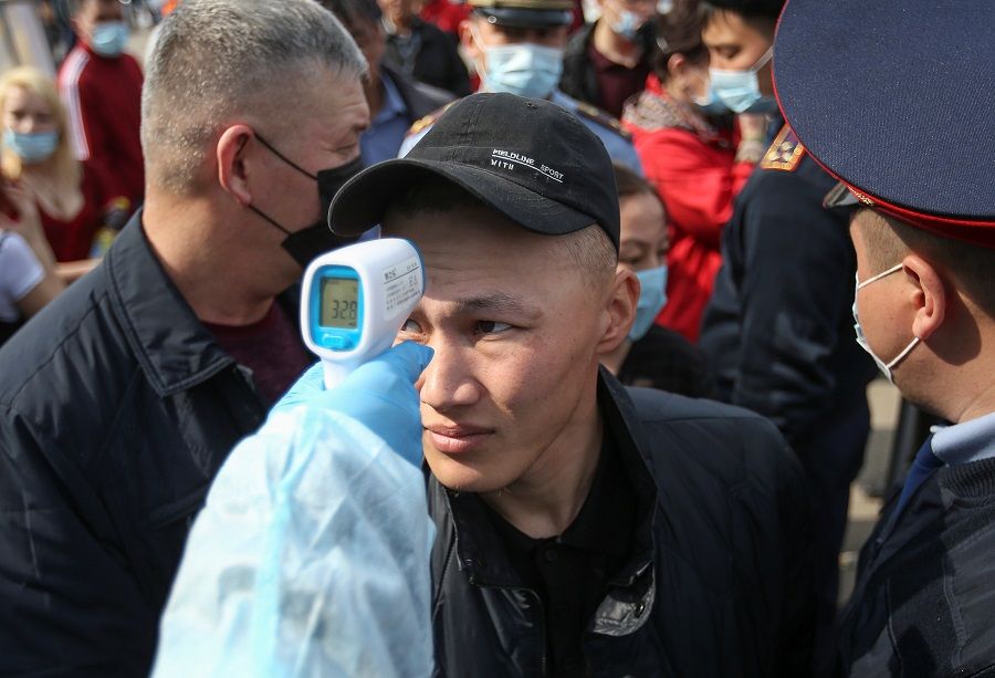 A medical official wearing protective gear takes the body temperature of a man who waits in line to enter the city following the Kazakh state emergency commission's decision to lock down Almaty at a checkpoint on the outskirts of Almaty, Kazakhstan, on 19 March 2020. (Pavel Mikheyev/Reuters)