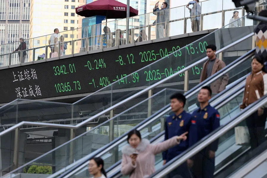 An electronic board shows Shanghai and Shenzhen stock indices as people walk on a pedestrian bridge at the Lujiazui financial district in Shanghai, China, on 3 April 2025. (Go Nakamura/Reuters)