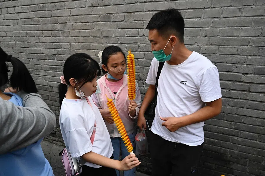 Two girls eat snacks in a commercial street during the country's national Golden Week holiday in Beijing, China on 2 October 2021. (Jade Gao/AFP)