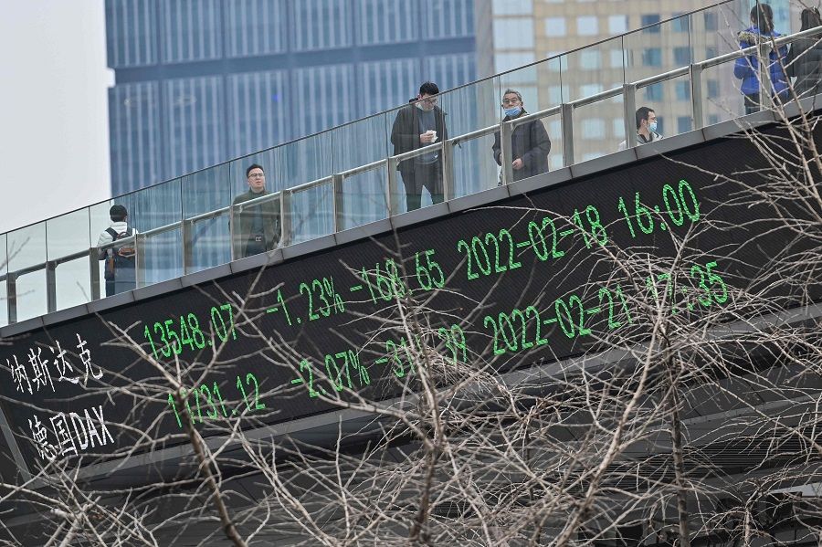 People walk across a bridge with a ticker board showing stock prices in the financial district of Shanghai, China, on 22 February 2022. (Hector Retamal/AFP)