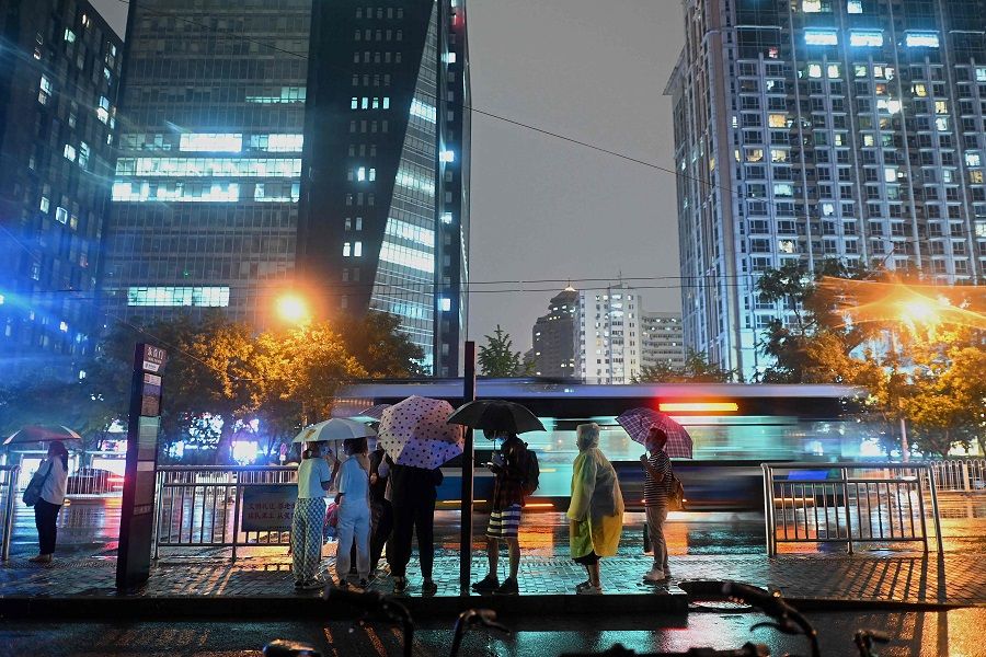 People wait for the bus as it rains in Beijing, China on 23 August 2021. (Noel Celis/AFP)
