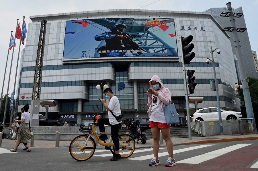 A large screen on a building showing promotion for the Chinese People's Liberation Army (PLA) is seen past pedestrians in Beijing, China, on 4 August 2022. (Noel Celis/AFP)