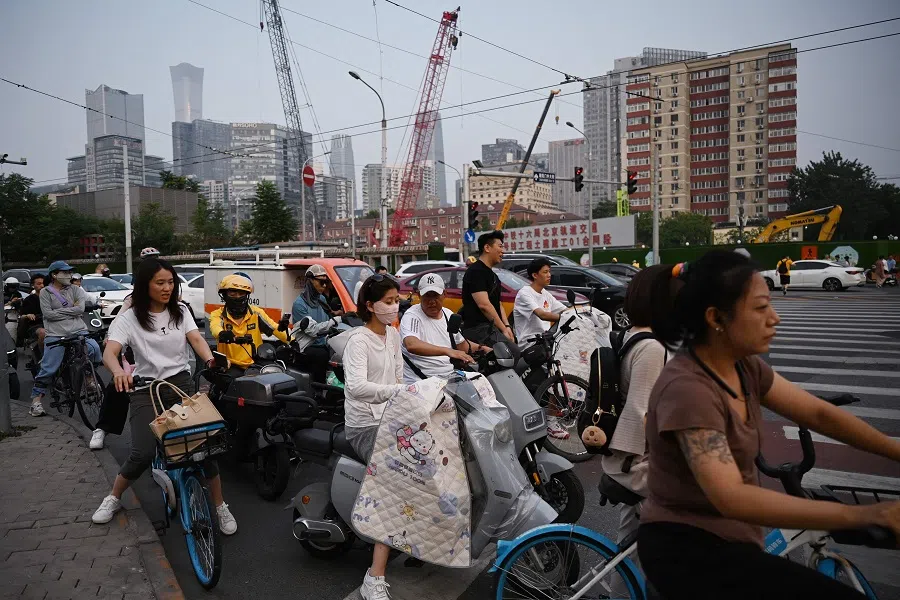 People wait to cross a road near a construction site in Beijing, China, on 9 July 2024.