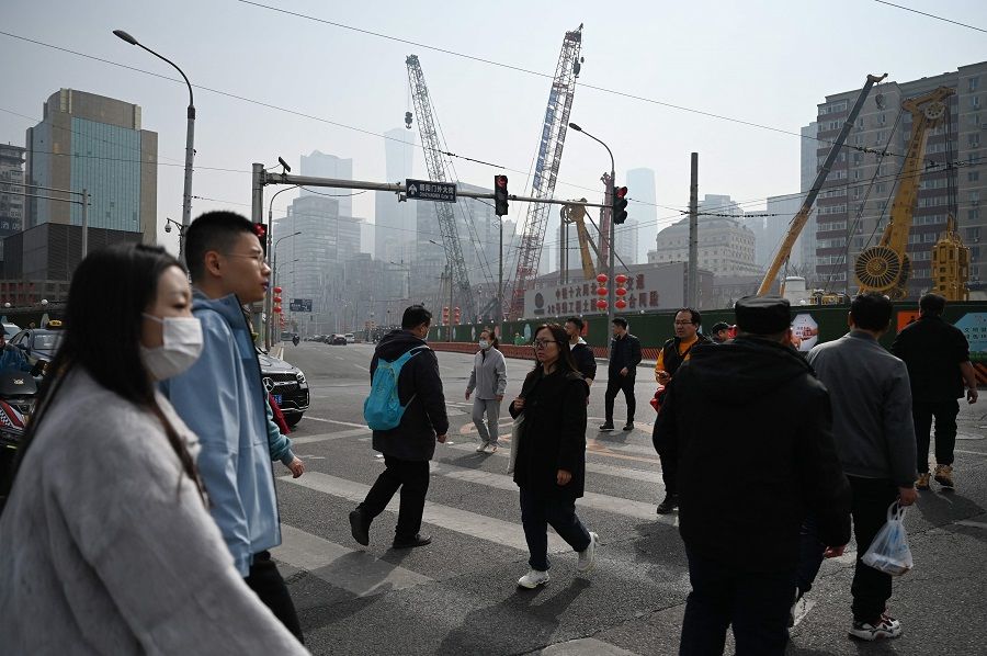 People cross a road in Beijing on 16 March 2024. (Greg Baker/AFP)