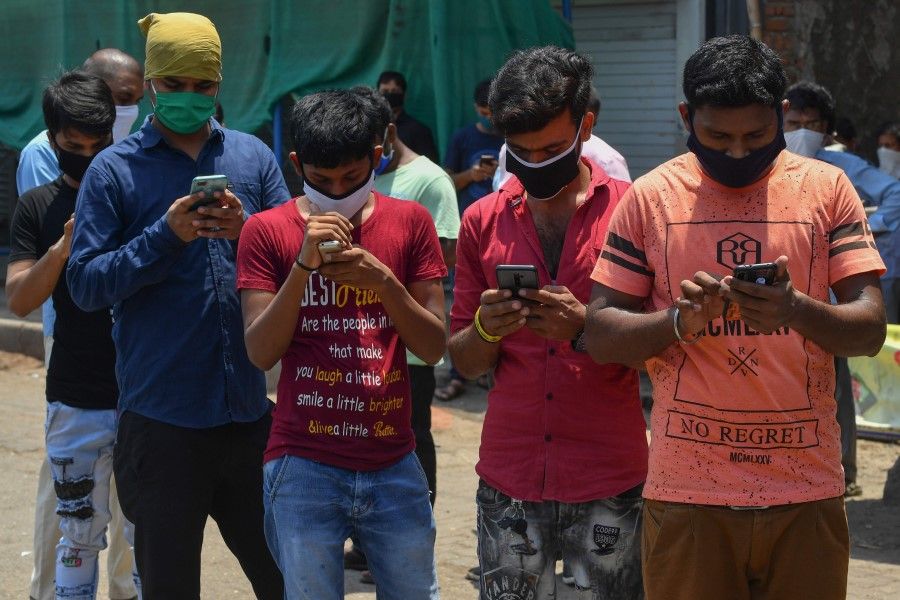 Migrant workers look at their mobile phones in Mumbai, 2 May 2020. (Indranil Mukherjee/AFP)