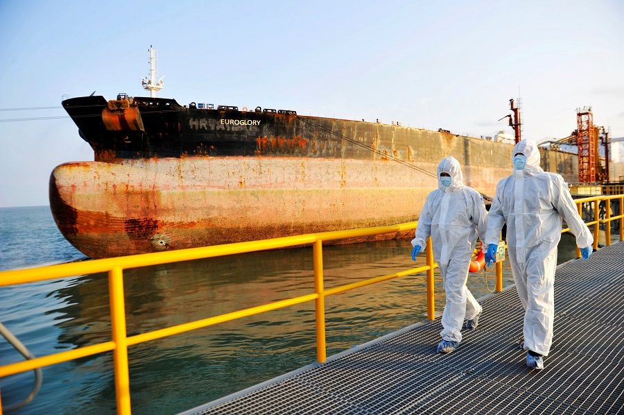 This photo taken on 16 November 2020 shows Chinese immigration inspection officers in protective suits walking past an oil tanker ship at the port in Qingdao, Shandong province, China. (STR/AFP)