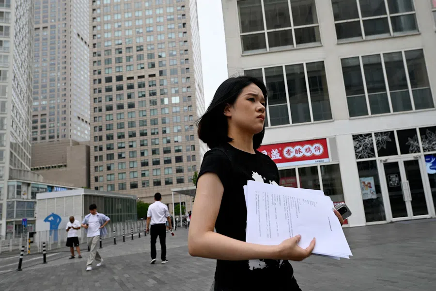 A woman holding papers walks past office buildings at the Central Business District (CBD) in Beijing, China, on 9 July, 2024.