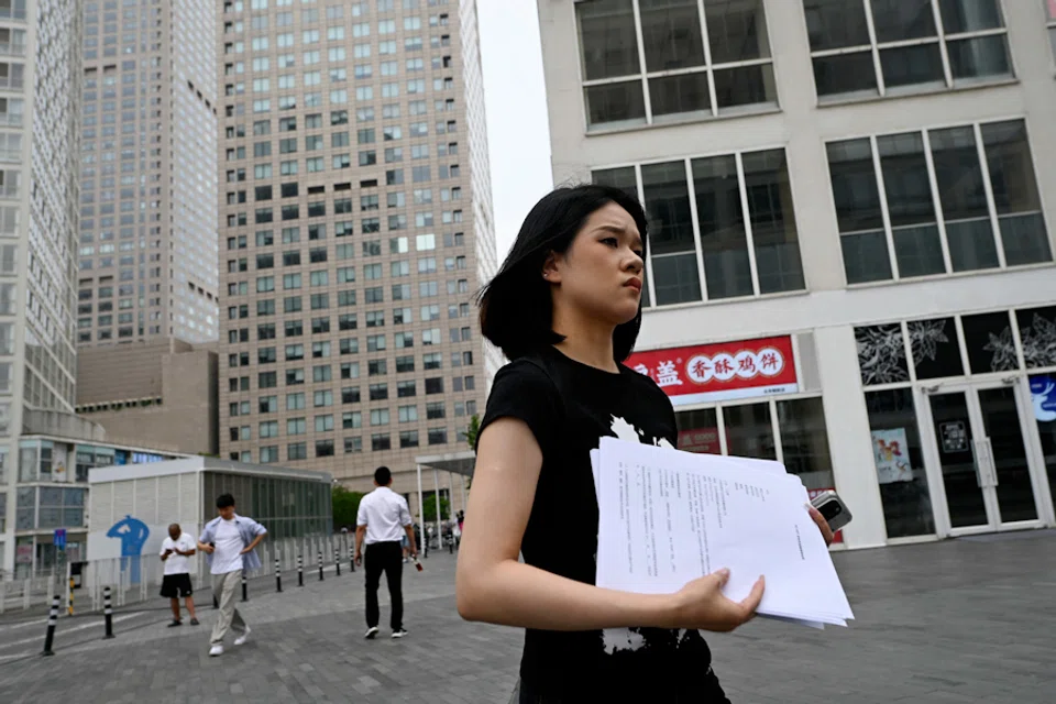A woman holding papers walks past office buildings at the Central Business District (CBD) in Beijing, China, on 9 July, 2024. (Wang Zhao/AFP)