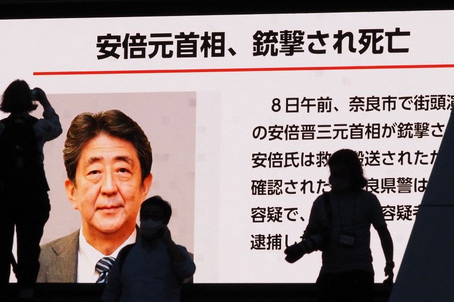 Pedestrians are silhouetted against a large public video screen showing an image of former Japanese prime minister Shinzo Abe in the Akihabara district of Tokyo on 8 July 2022, after he was shot and killed in the city of Nara. (Toshifumi Kitamura/AFP)