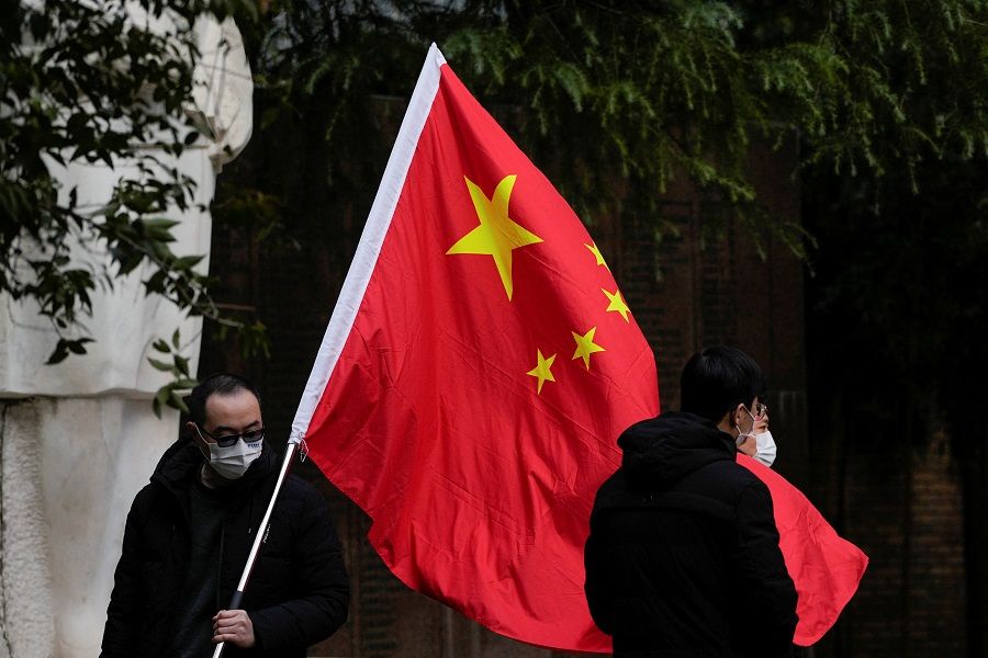 People wearing face masks pose for photos with a Chinese national flag at a park in Shanghai, China, 12 December 2022. (Aly Song/Reuters)
