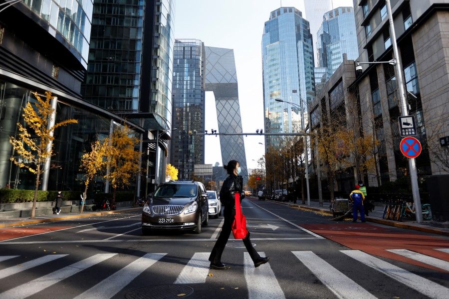 A woman walks across the street during morning rush hour, following the outbreak of the coronavirus disease (COVID-19), in the Central Business District (CBD) in Chaoyang District, Beijing, China, 21 November 2022. (Tingshu Wang/Reuters)