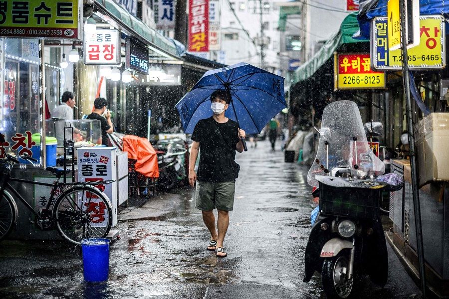 A man uses an umbrella to shield himself from the rain while walking past shops along a street during a downpour in Seoul, South Korea, on 30 June 2022. (Anthony Wallace/AFP)