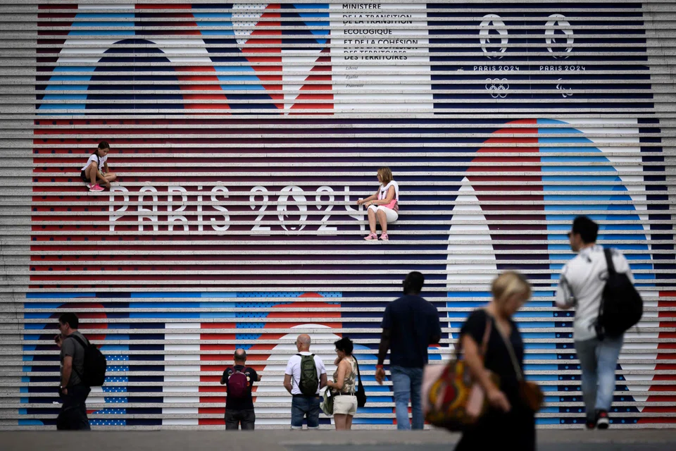 People pose on stairs near the logo of Paris 2024 Olympics Olympic games a few days before the opening ceremony, at La Defense business district, West of Paris, on 22 July 2024. (Loic Venance/AFP)