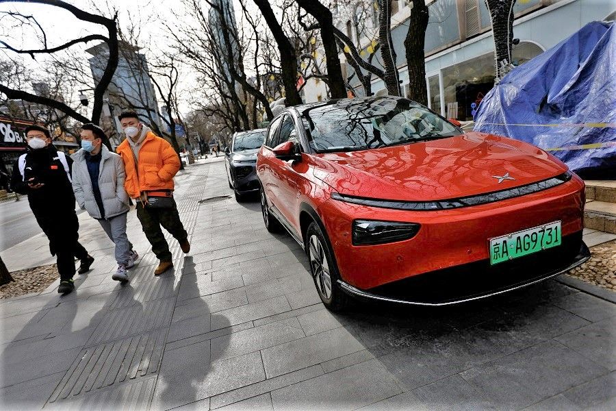 People walk past an XPeng electric vehicle (EV) in front of its flagship store in Beijing, China, 2 February 2023. (Tingshu Wang/Reuters)