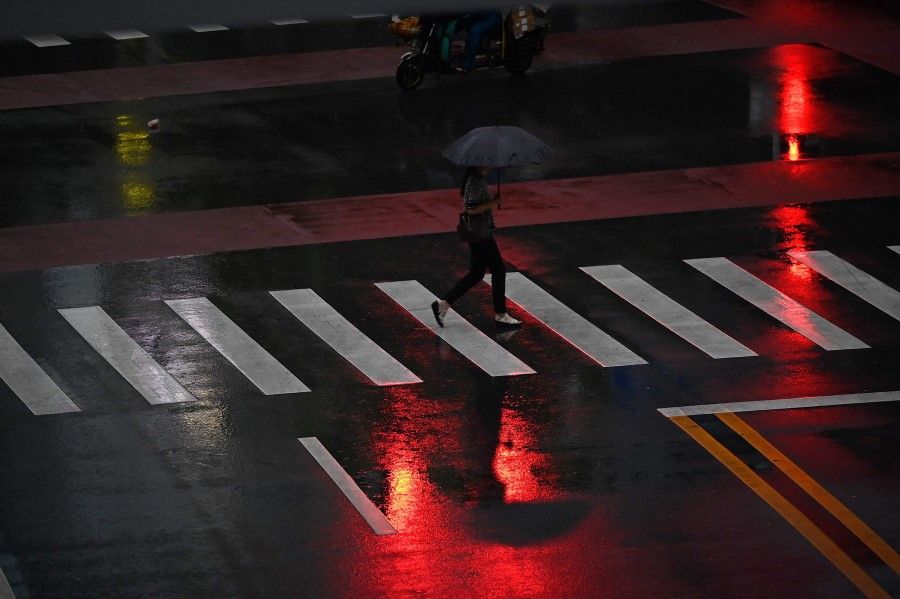 A woman walks on a pedestrian crossing on a rainy day in Beijing on 19 August 2021. (Jade Gao/AFP)