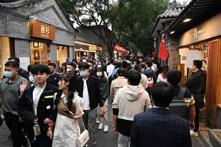 People walk in a commercial street named Nanluoguxiang during the country's national Golden Week holiday in Beijing on 2 October 2021. (Jade Gao/AFP)