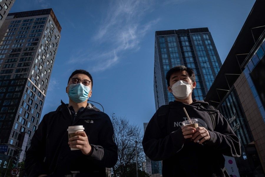 Two men hold their Starbucks beverages as they cross a street in Beijing, April 22, 2020. (Nicolas Asfouri/AFP)