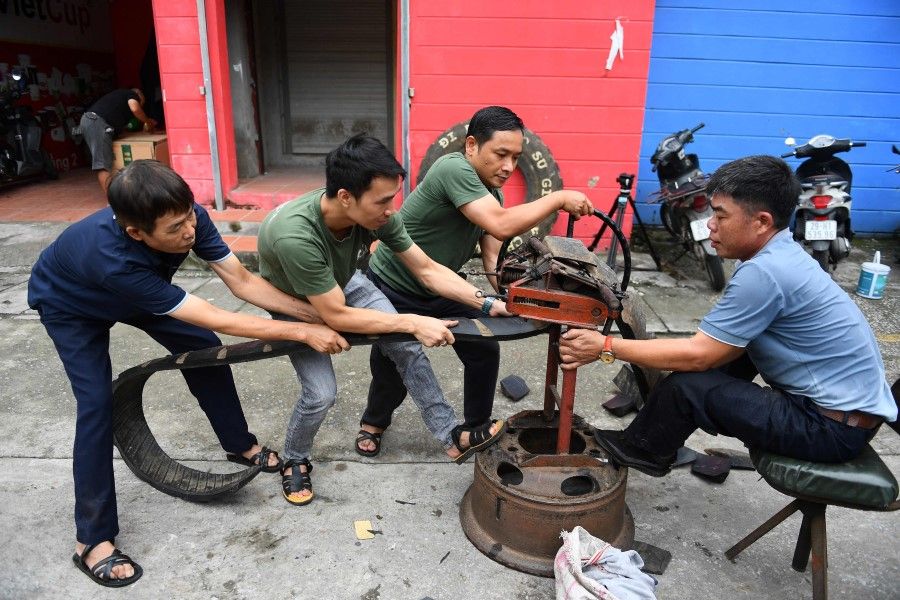 This photo taken on 8 July 2022 shows workers cutting apart a rubber truck tyre outside a workshop in Hanoi. (Nhac Nguyen/AFP)