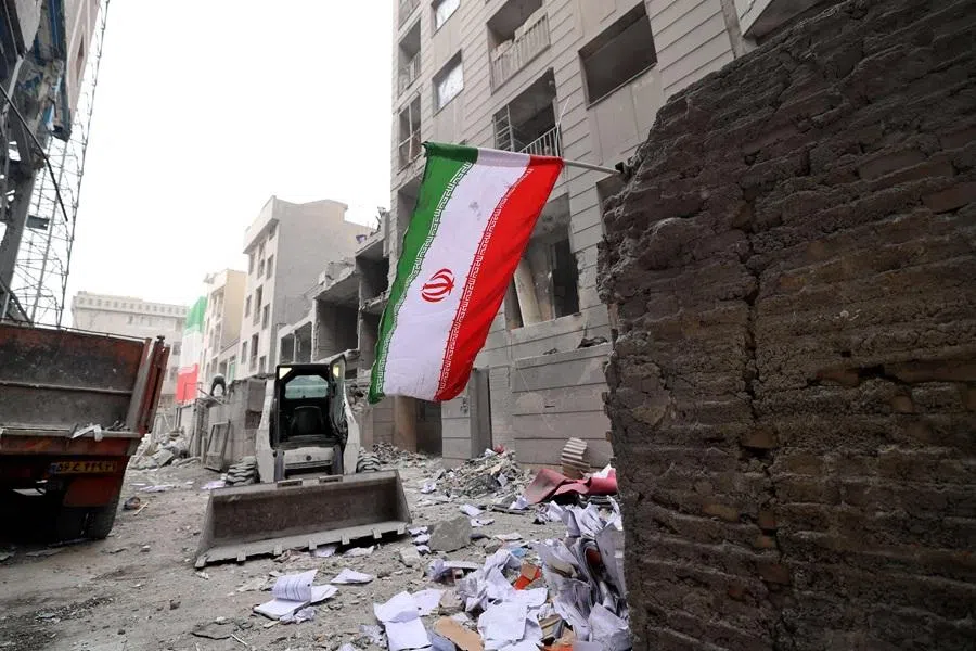 An Iranian flag flutters as a digger arrives to help remove the debris from destroyed buildings following a military strike on the Iranian capital of Tehran on 15 March 2026. (Atta Kenare/AFP)